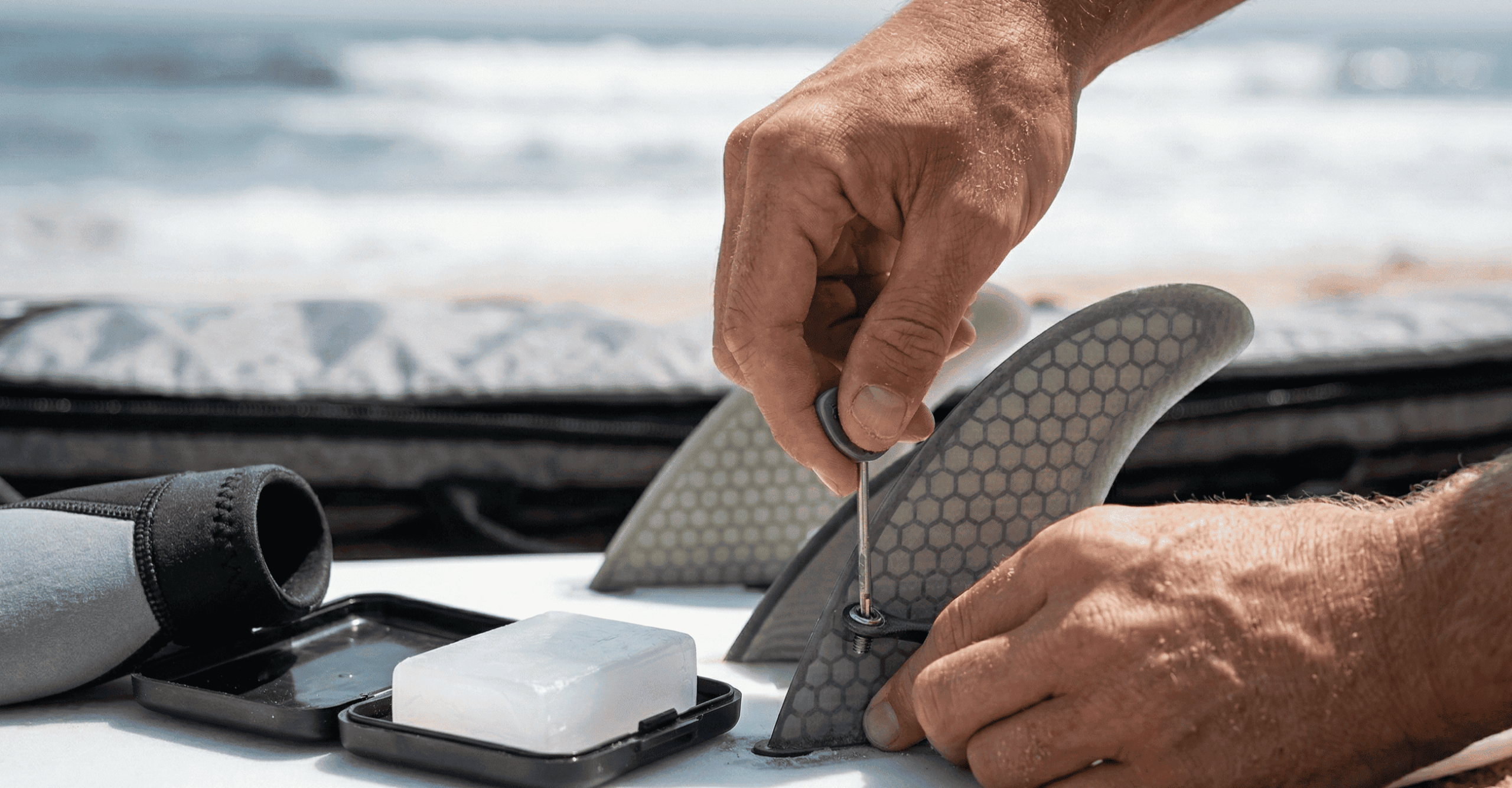Best Surf Gear for Intermediate Surfers: A close-up, macro shot on the beach captures hands installing stiff, honeycombed fiberglass and carbon-composite Futures fins