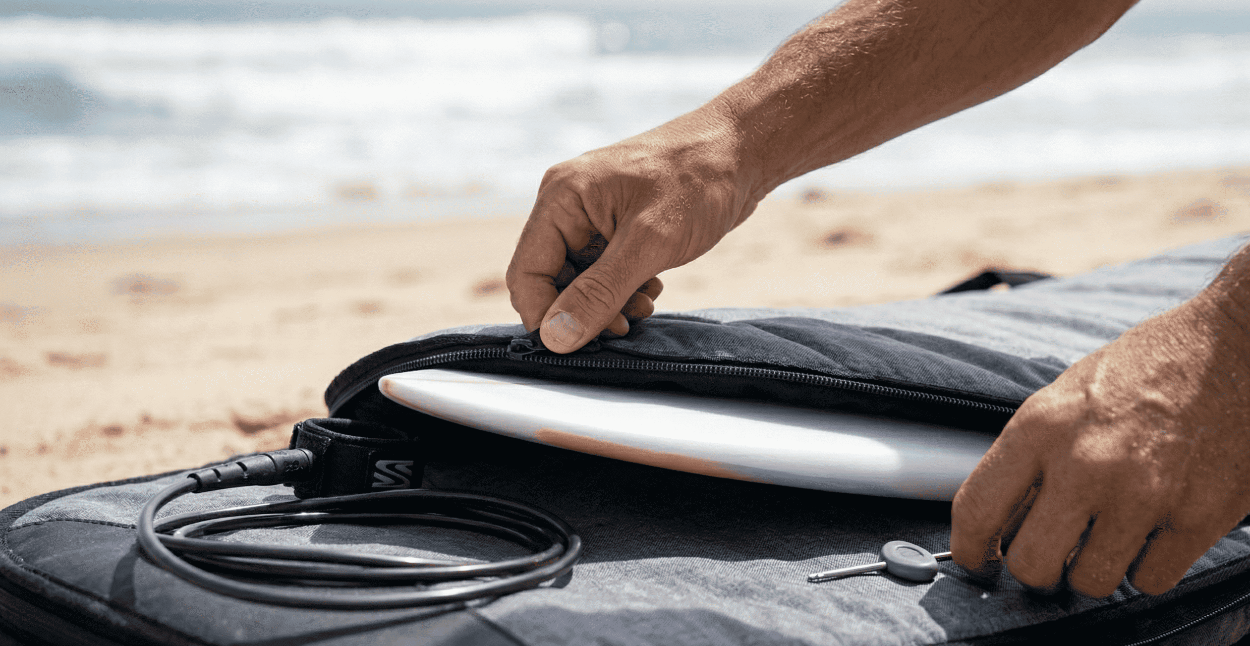 Illustrating the travel-readiness section, this image focuses on proper board protection. It features a horizontal close-up shot on the beach where a focused surfer is zipping their polished 6'10" hybrid board